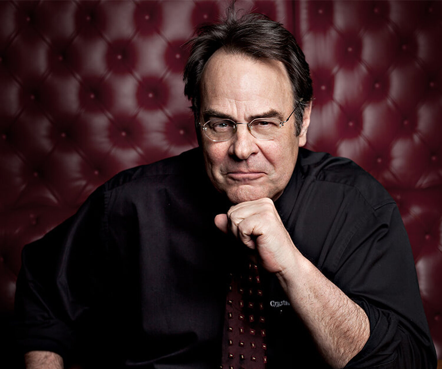 Dan Aykroyd poses for a headshot in a burgundy leather booth